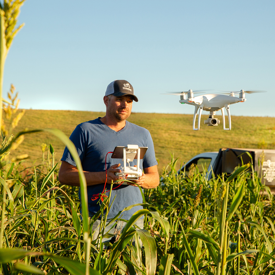 Brandon Bunn flying a white quadcopter drone over a field