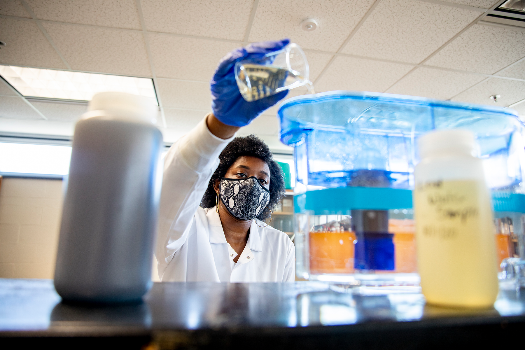 Image of a female scientist pouring water into a container from a beaker.