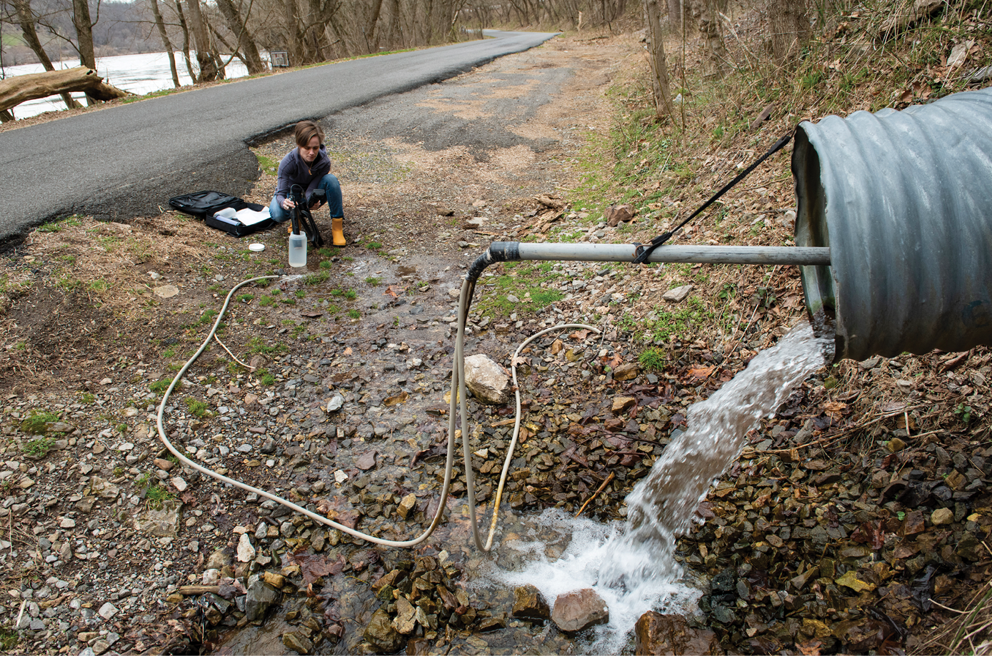 Image of Leigh-Anne Krometis crouched down inspectingn water coming from a pipe